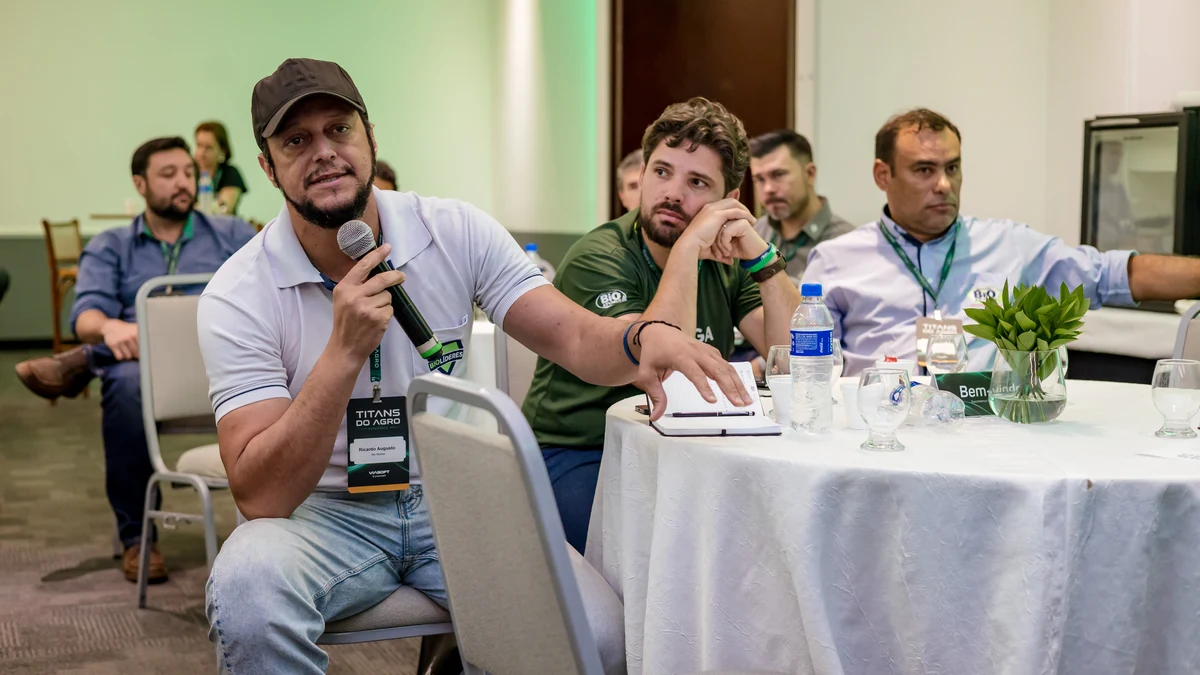 Participante sentado à mesa redonda faz uma pergunta ao microfone enquanto os demais acompanham