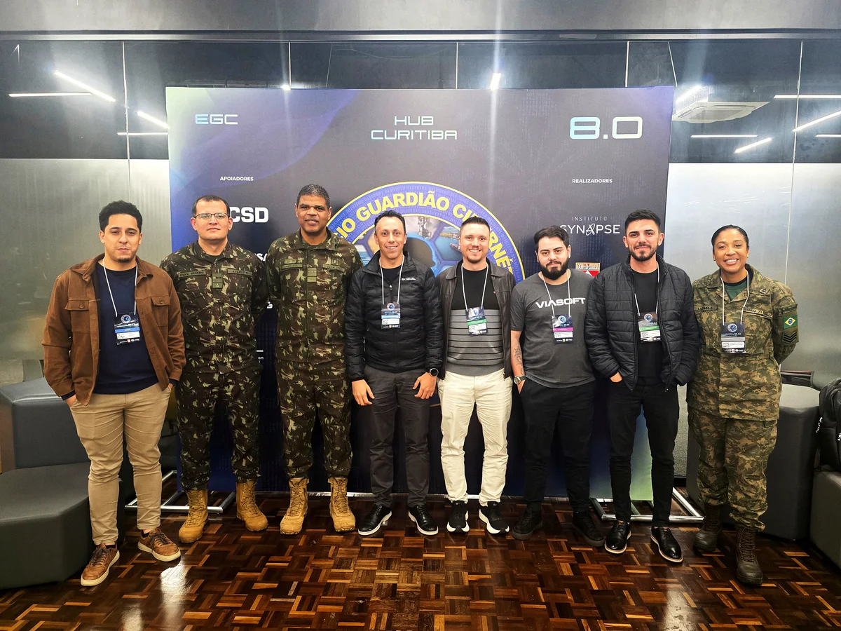Equipe da VIASOFT ao lado de militares do Exército Brasileiro diante do painel do Exercício Guardião Cibernético 8.0, no hub de Curitiba